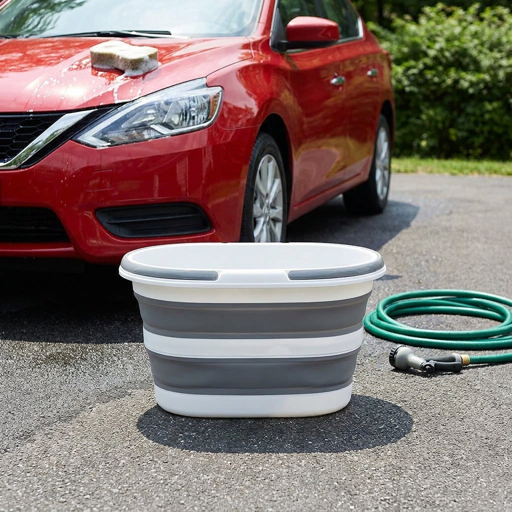 Portable folding car wash basin bucket beside a car with a hose and sponge on a sunny driveway
