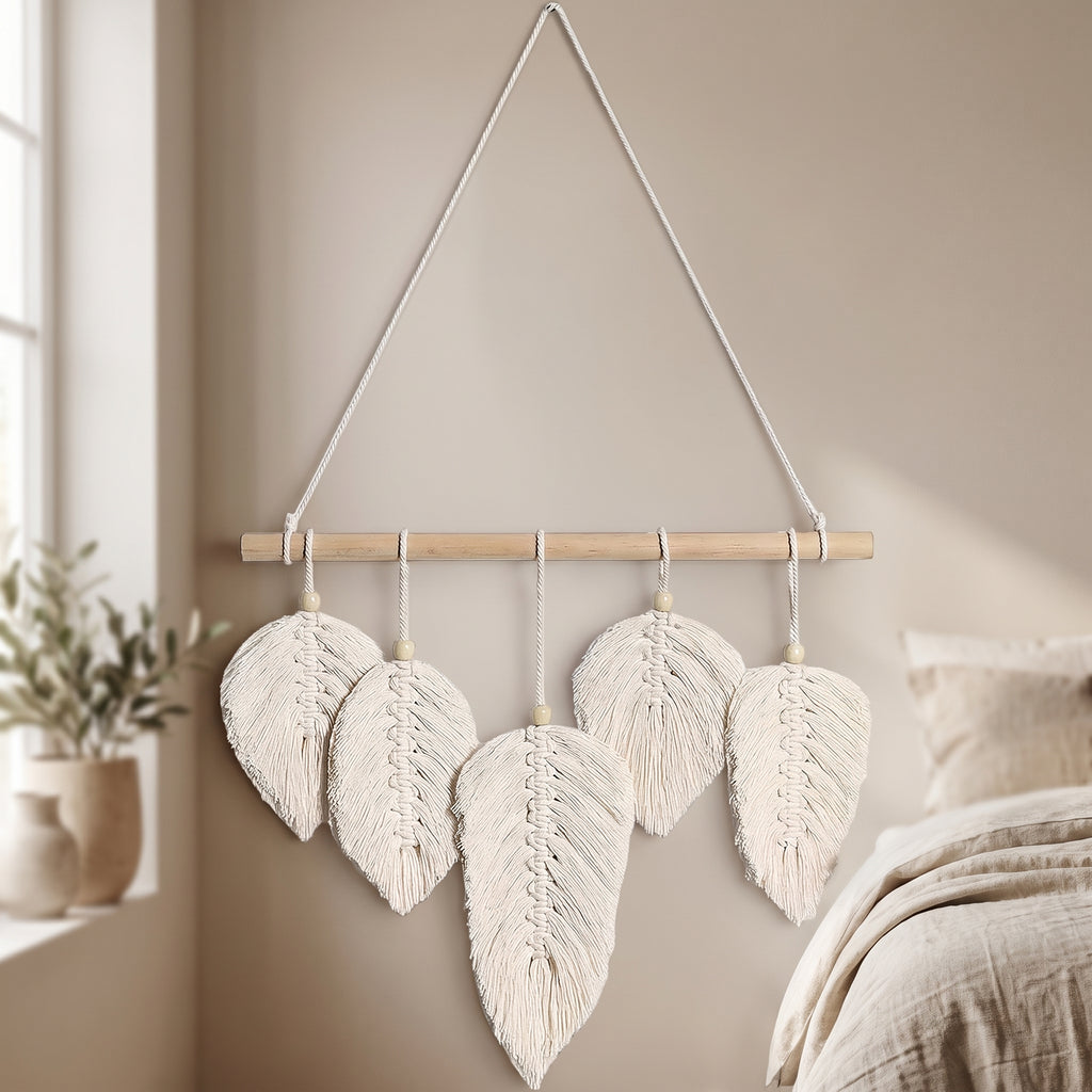 Cream macrame leaf wall hanging with five woven leaves on a wooden dowel, mounted on a bedroom wall