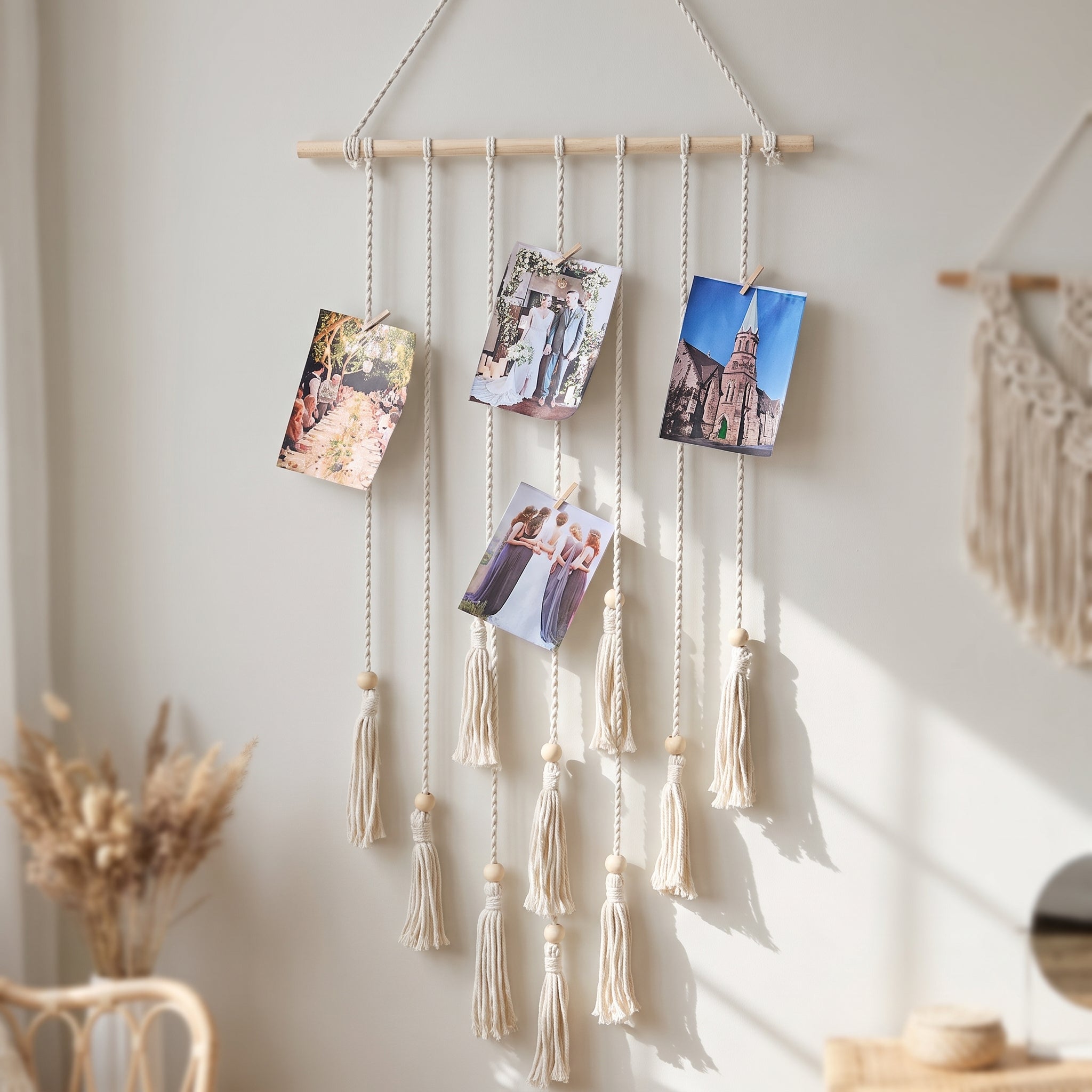 Macrame photo display wall hanging with clipped photos and tassels mounted on a bright bedroom wall