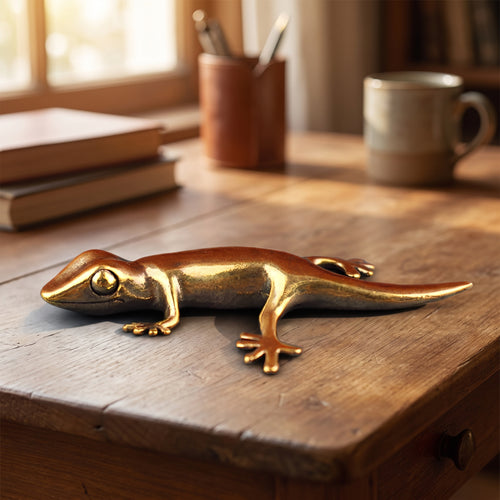 Antique brass gecko figurine ornament resting on a wooden desk