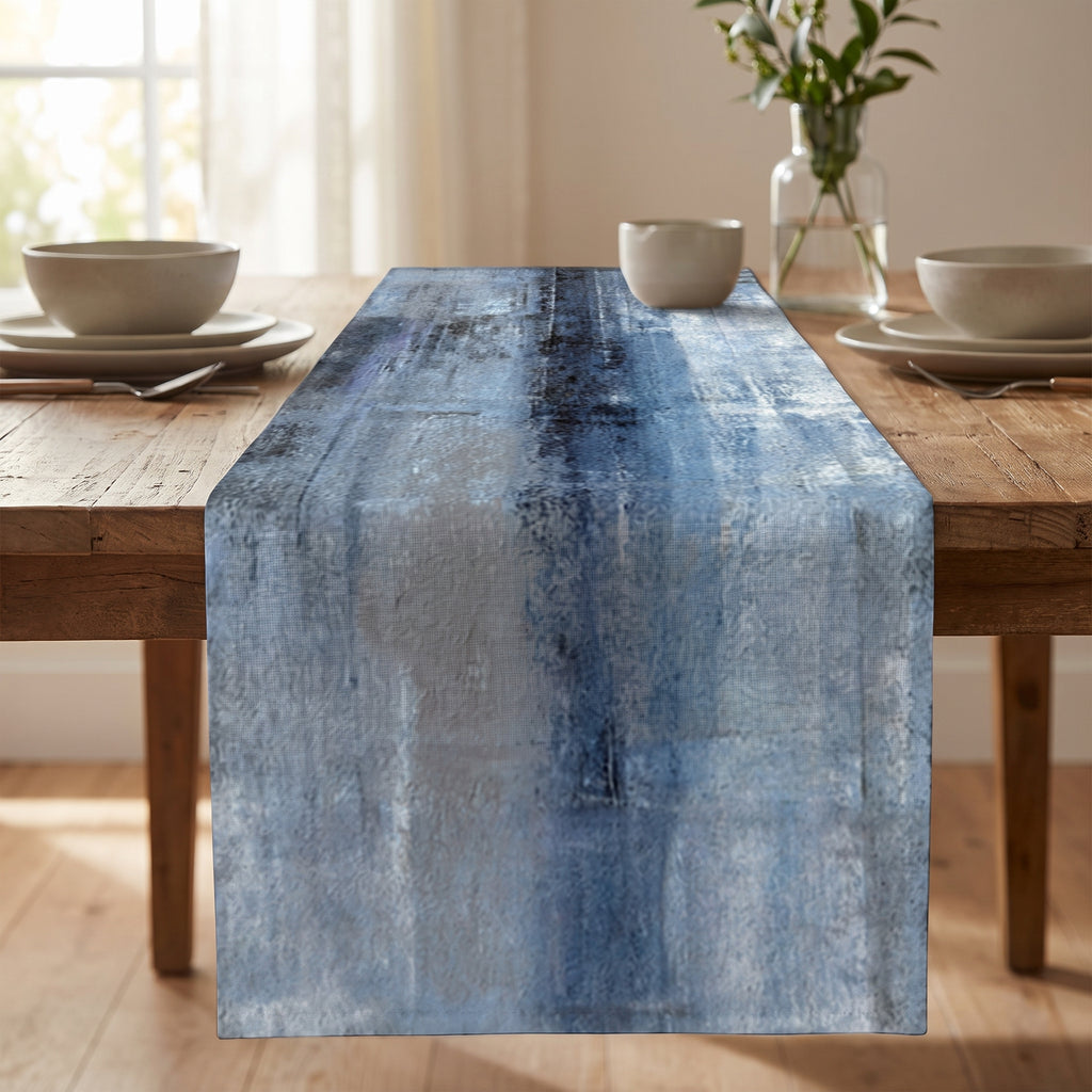 Blue and white abstract-dyed linen table runner styled on a rustic wooden dining table with neutral dinnerware