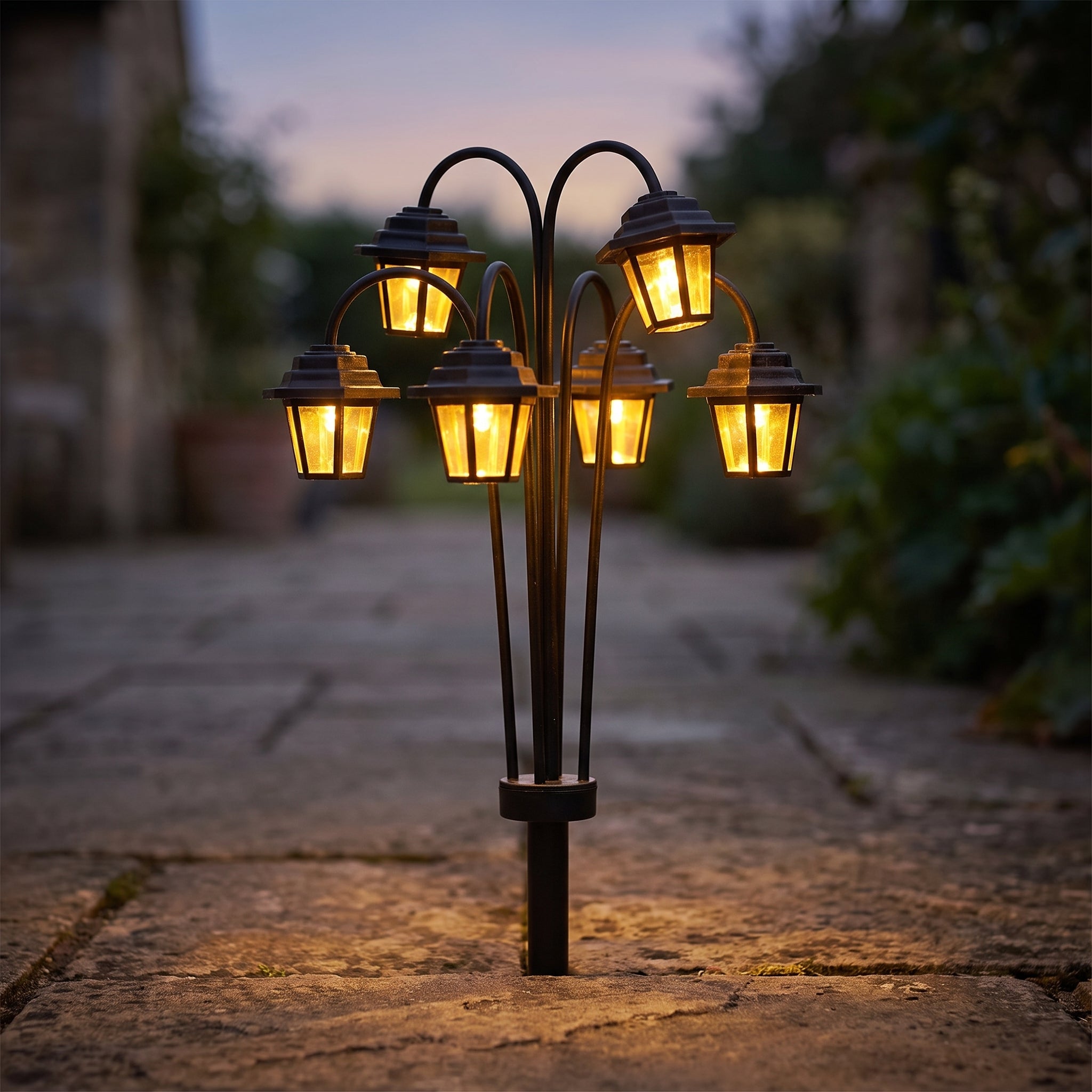 Solar-powered retro street lamp shaped garden lantern with six glowing LED lamp heads staked in a stone courtyard path at dusk