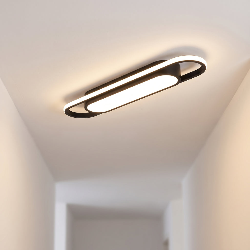 Black rectangular LED strip ceiling light illuminating a modern minimalist hallway with warm white light