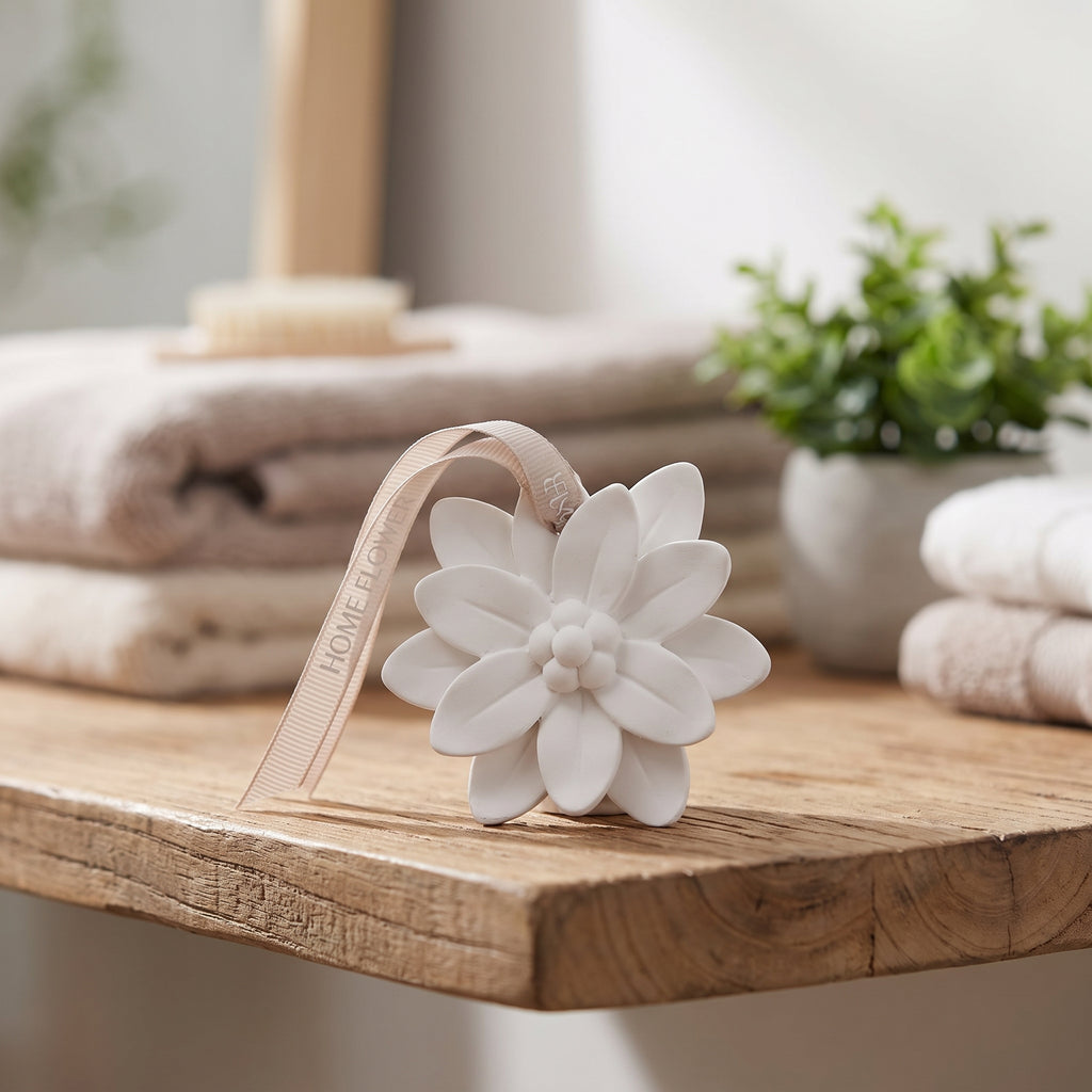 White ceramic flower-shaped aromatherapy diffuser with hanging ribbon on a wooden bathroom shelf