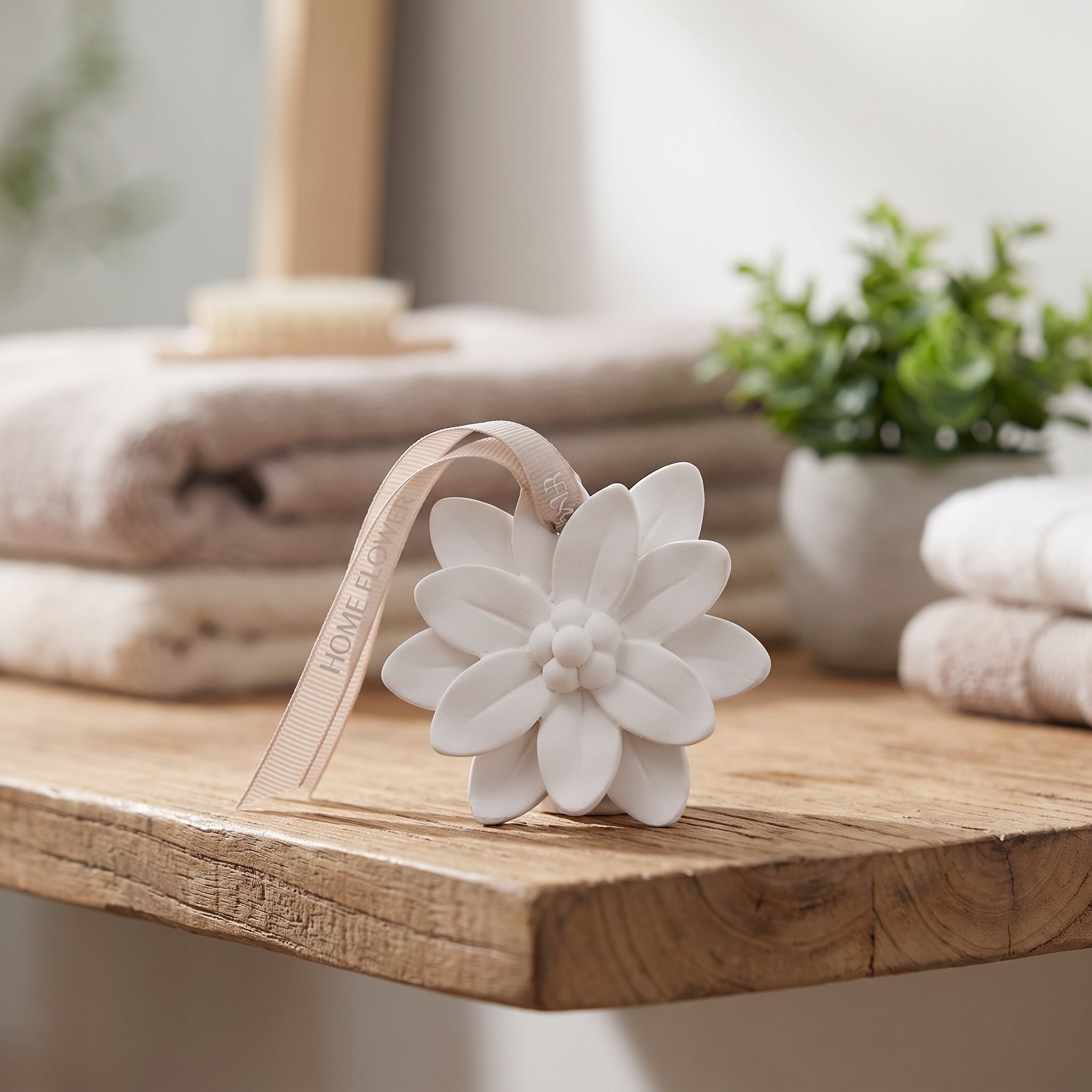White ceramic flower-shaped aromatherapy diffuser with hanging ribbon on a wooden bathroom shelf
