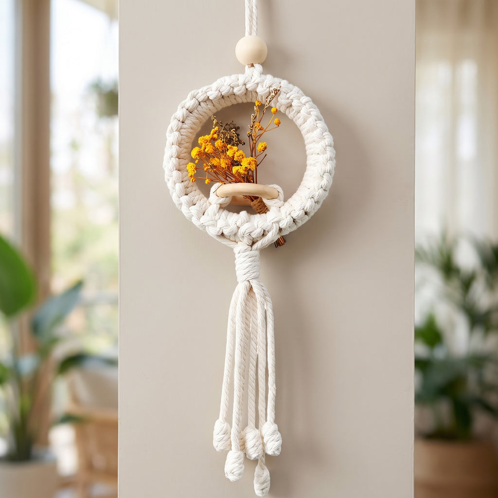 Cream macrame ring air plant holder with a small dried flower arrangement mounted on a wall